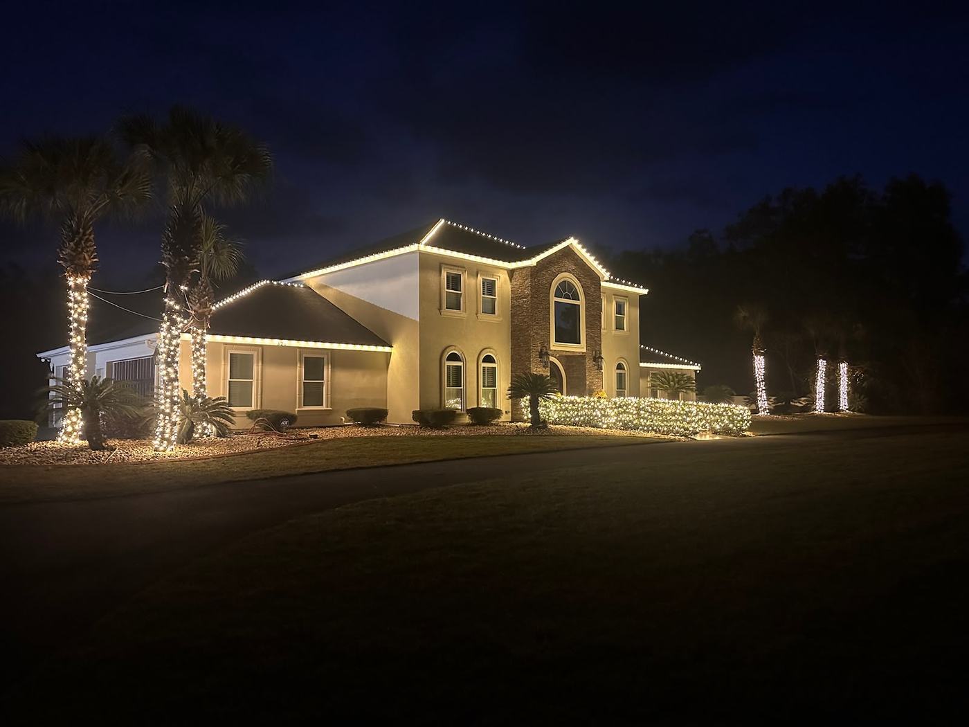 Warm white roofline lighting and wrapped trees on a stucco home